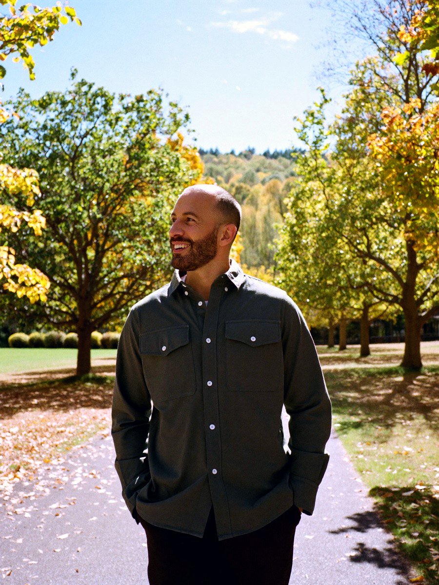 A man walking a sunlit tree-lined path, unhurried